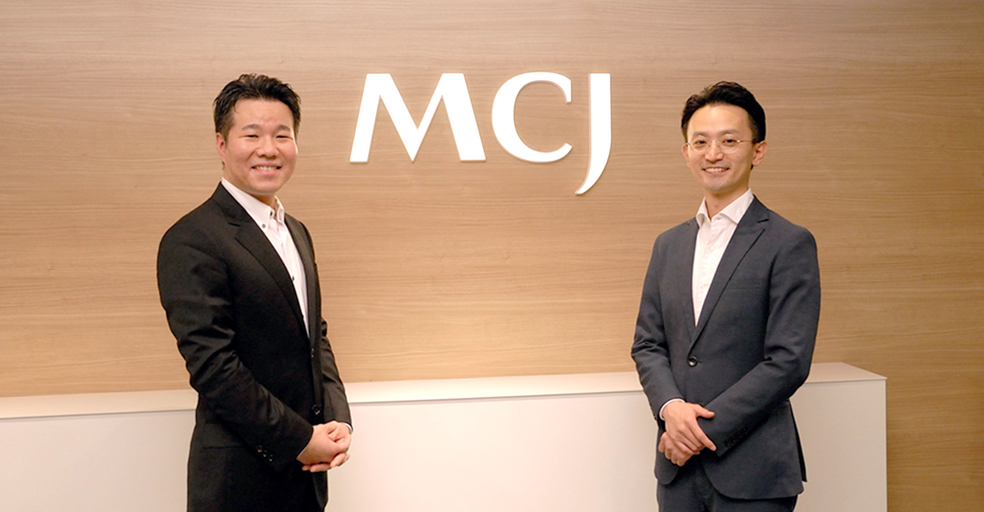 株式会社MCJのロゴの前で笑顔の代表取締役 安井氏と聞き手、野村アセットマネジメント株式会社 馮